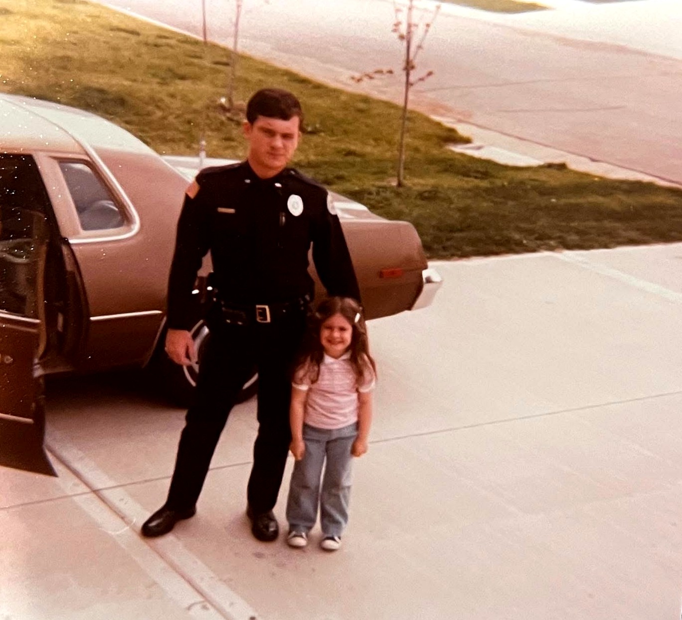 Holly as a young girl standing with her dad in uniform beside his car